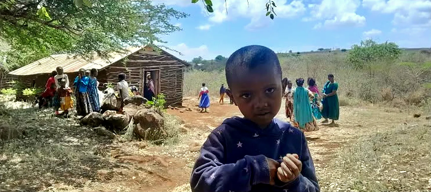 A young boy looking into the camera outside the timber church, parishioners gathered behind him.